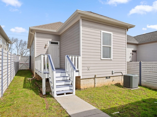 back of house featuring cooling unit, roof with shingles, a fenced backyard, crawl space, and a lawn