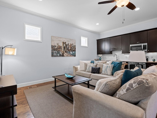 living room featuring a ceiling fan, baseboards, recessed lighting, ornamental molding, and light wood-style floors