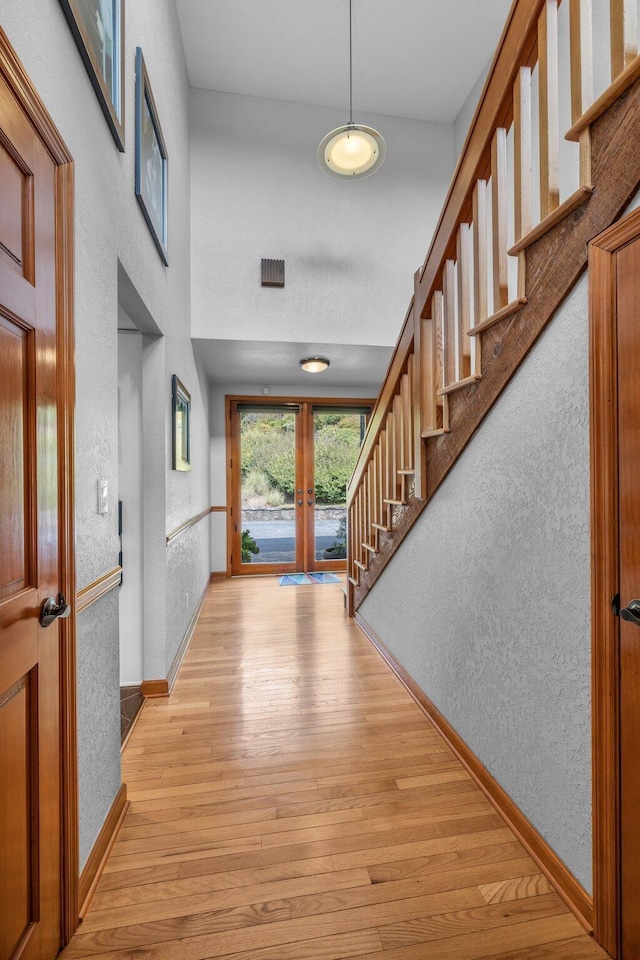 foyer entrance with stairway, baseboards, light wood finished floors, french doors, and a textured wall