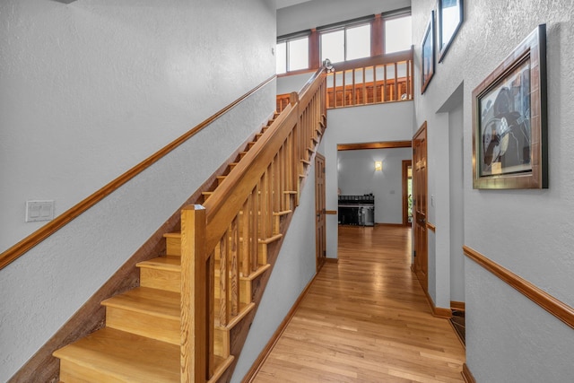 staircase featuring baseboards, a towering ceiling, and wood finished floors