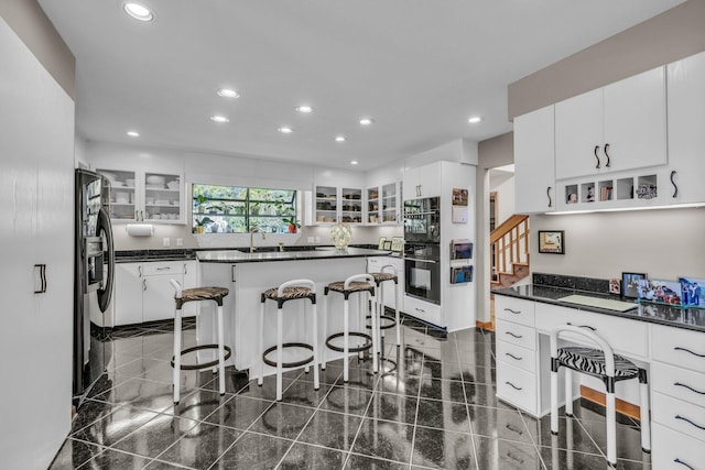 kitchen featuring recessed lighting, glass insert cabinets, dark countertops, and a breakfast bar