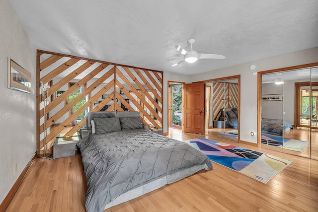 bedroom with a ceiling fan, baseboards, multiple closets, wood-type flooring, and a textured ceiling