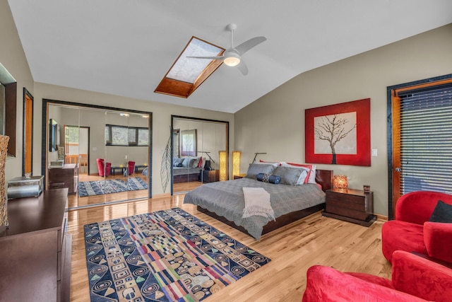 bedroom with ceiling fan, lofted ceiling with skylight, two closets, and wood finished floors