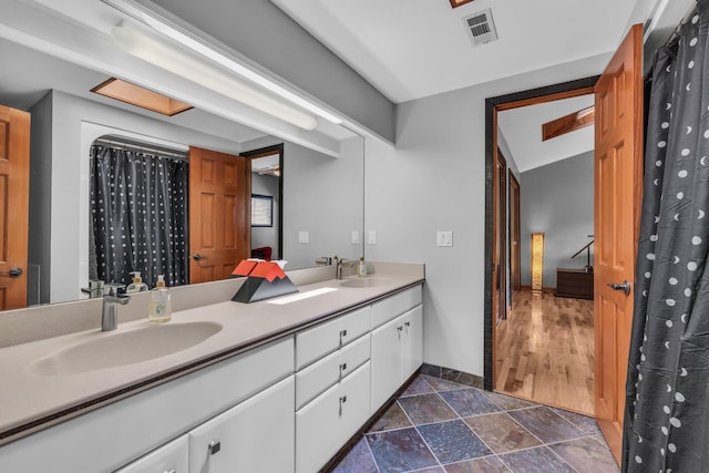 bathroom featuring a sink, visible vents, stone tile floors, and double vanity