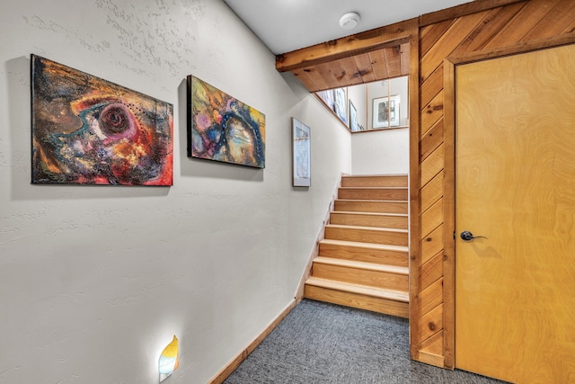 stairway with beam ceiling, baseboards, and carpet