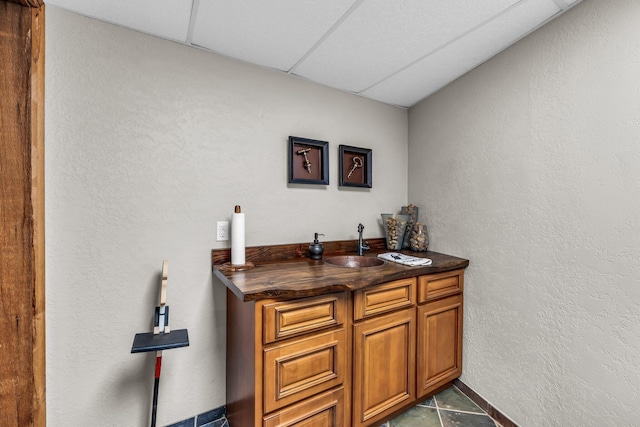 bar featuring a sink, indoor wet bar, a paneled ceiling, and a textured wall