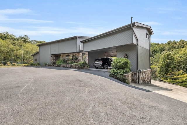 view of side of property featuring aphalt driveway, stone siding, and a carport