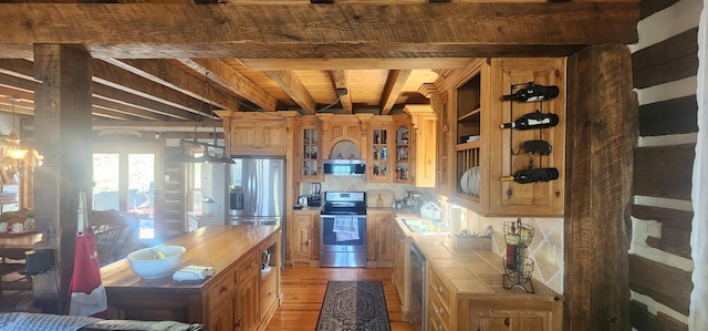 kitchen featuring beam ceiling, light wood-style flooring, a sink, tile counters, and appliances with stainless steel finishes