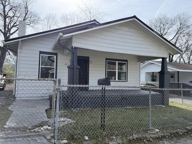 shotgun-style home featuring an attached carport, a gate, covered porch, a chimney, and a fenced front yard