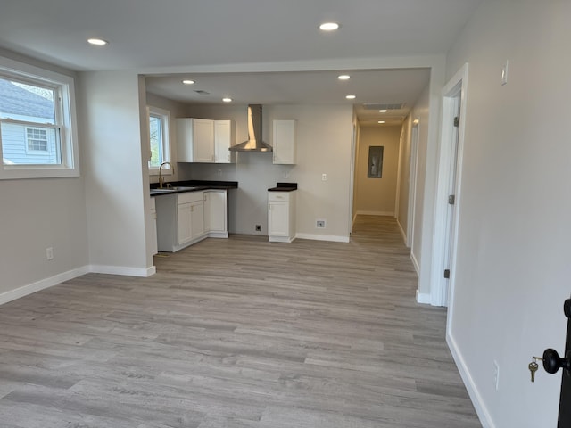 kitchen with a sink, white cabinets, recessed lighting, and wall chimney range hood