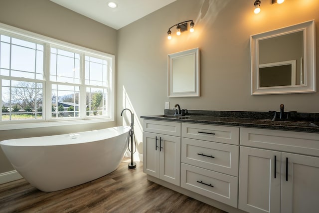 full bath featuring a sink, a freestanding bath, wood finished floors, and double vanity