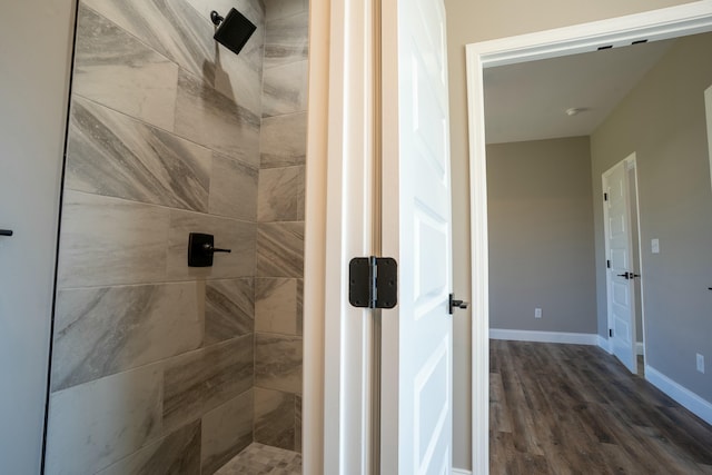 full bath featuring a tile shower, baseboards, and wood finished floors