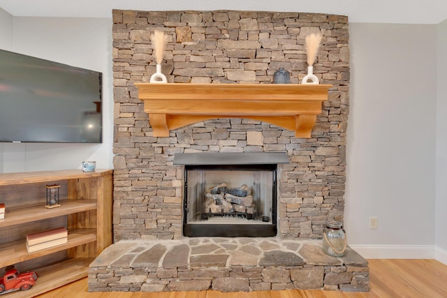 interior details with baseboards, a stone fireplace, and wood finished floors