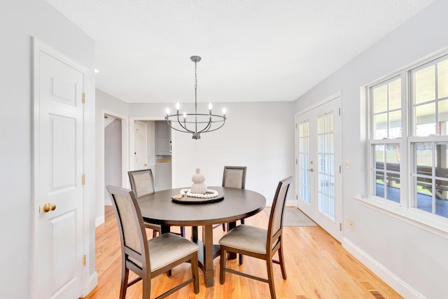 dining area with light wood finished floors, visible vents, an inviting chandelier, and baseboards