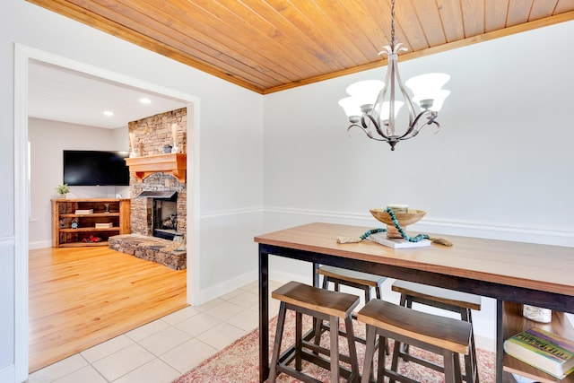 dining space with baseboards, light tile patterned floors, wooden ceiling, a fireplace, and a notable chandelier