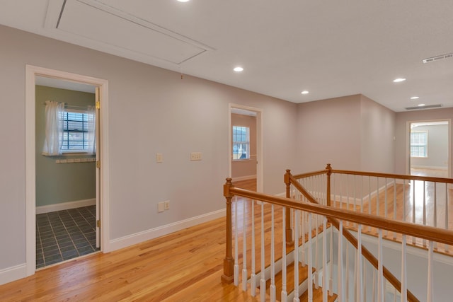 hallway with visible vents, light wood finished floors, baseboards, attic access, and an upstairs landing