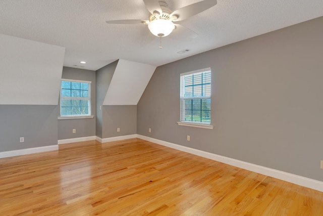 additional living space with a textured ceiling, a healthy amount of sunlight, light wood-style floors, and baseboards