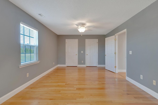 unfurnished room featuring visible vents, baseboards, light wood-style floors, and a textured ceiling