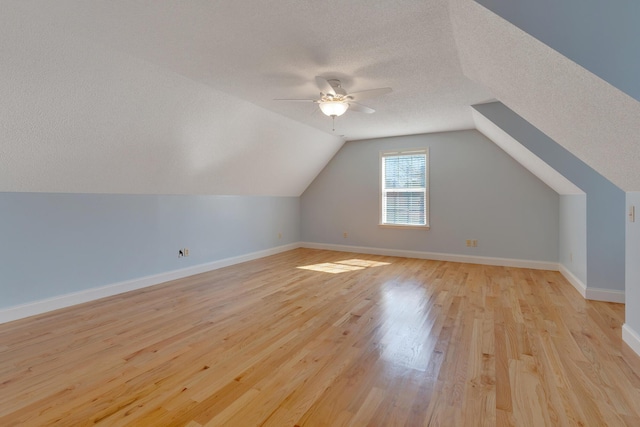 additional living space with lofted ceiling, a ceiling fan, a textured ceiling, light wood finished floors, and baseboards