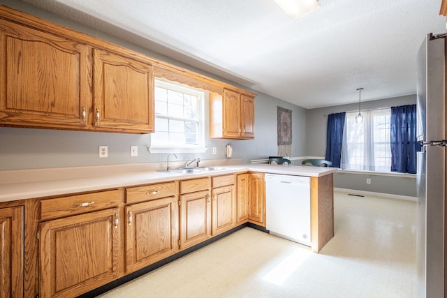 kitchen with a sink, freestanding refrigerator, a peninsula, a healthy amount of sunlight, and dishwasher