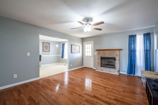 unfurnished living room featuring a ceiling fan, wood finished floors, baseboards, a textured ceiling, and a brick fireplace