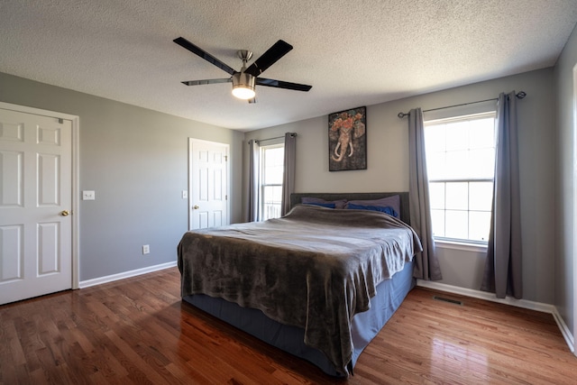 bedroom with visible vents, baseboards, wood finished floors, a textured ceiling, and a ceiling fan