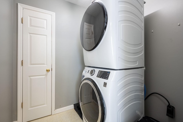 laundry room with laundry area, light floors, stacked washing maching and dryer, and baseboards