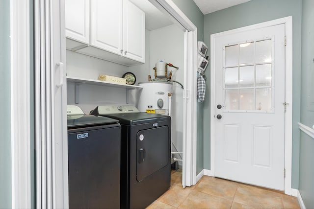 clothes washing area featuring baseboards, washing machine and dryer, water heater, light tile patterned flooring, and cabinet space