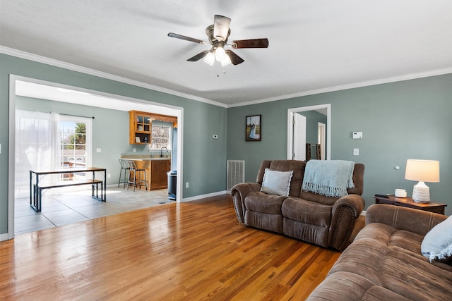 living area featuring visible vents, baseboards, ornamental molding, wood finished floors, and a ceiling fan