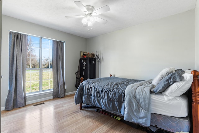 bedroom featuring a ceiling fan, baseboards, visible vents, a textured ceiling, and light wood-type flooring