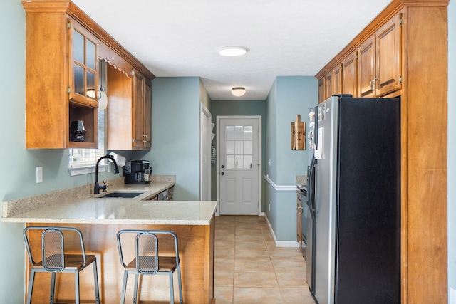 kitchen featuring fridge with ice dispenser, a sink, a peninsula, light tile patterned floors, and glass insert cabinets