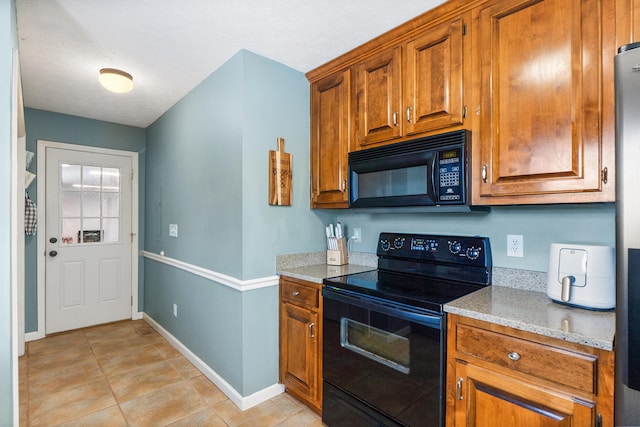 kitchen with black appliances, light stone counters, light tile patterned flooring, brown cabinetry, and baseboards