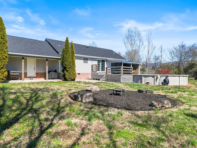 back of property featuring a yard, an outdoor fire pit, a deck, and roof with shingles