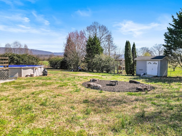 view of yard featuring an outbuilding, a shed, a mountain view, a fire pit, and an outdoor pool