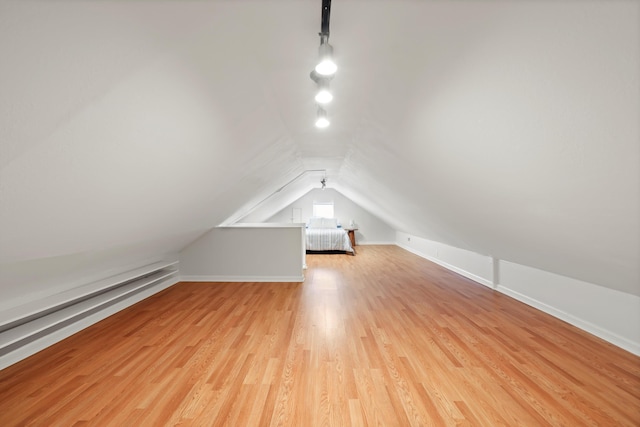 additional living space with light wood-style flooring, baseboards, lofted ceiling, and a baseboard radiator