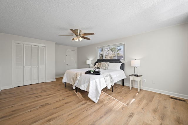 bedroom featuring visible vents, light wood-style flooring, a textured ceiling, baseboards, and ceiling fan