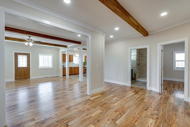 unfurnished living room featuring light wood finished floors, beamed ceiling, a fireplace, and a wealth of natural light