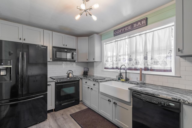 kitchen with black appliances, a sink, backsplash, stone counters, and a chandelier