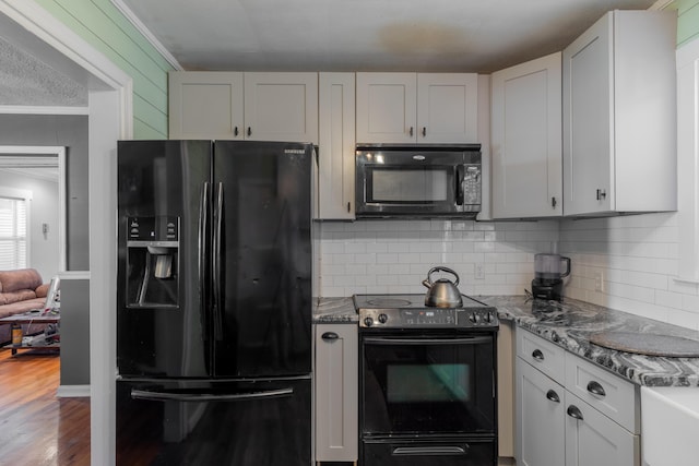 kitchen with wood finished floors, dark stone counters, ornamental molding, decorative backsplash, and black appliances