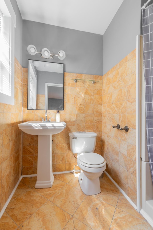 full bathroom featuring tile patterned floors, toilet, a sink, curtained shower, and tile walls