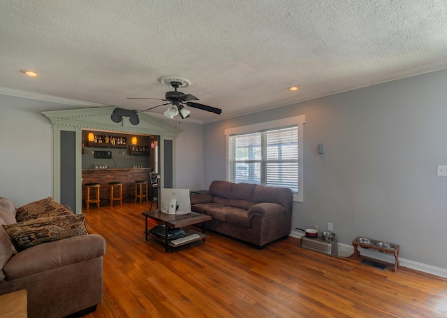 living area featuring crown molding, baseboards, a dry bar, wood finished floors, and a ceiling fan