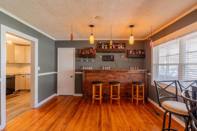 bar featuring visible vents, light wood-style flooring, a dry bar, and ornamental molding