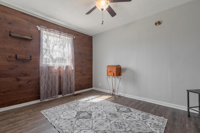 interior space featuring baseboards, wood finished floors, ceiling fan, and wood walls