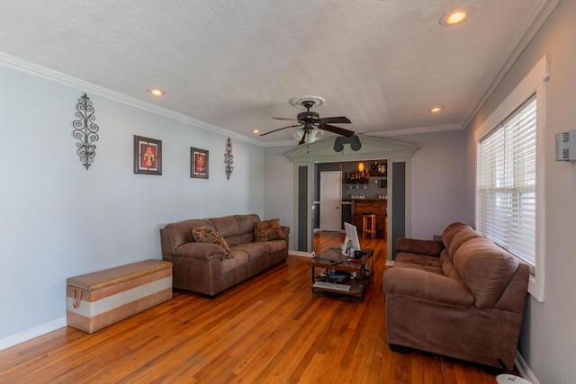 living room featuring a textured ceiling, crown molding, a ceiling fan, and wood finished floors