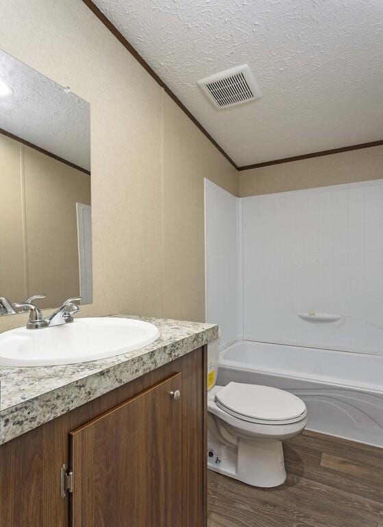 full bathroom with visible vents, toilet, vanity, wood finished floors, and a textured ceiling