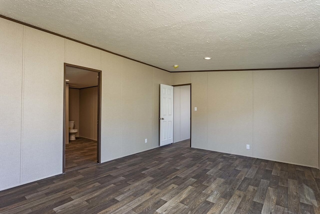 spare room featuring a textured ceiling, dark wood-type flooring, crown molding, and a decorative wall