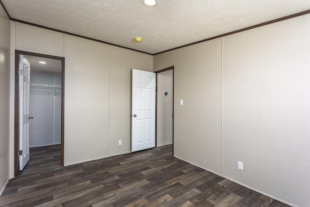 unfurnished bedroom with a spacious closet, crown molding, a closet, a textured ceiling, and dark wood-style flooring