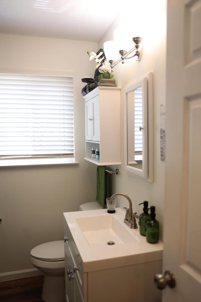 half bathroom with vanity, toilet, and baseboards