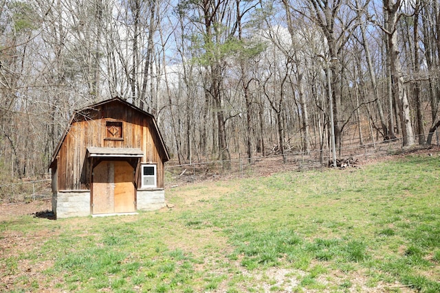 view of barn featuring a view of trees, a yard, and fence