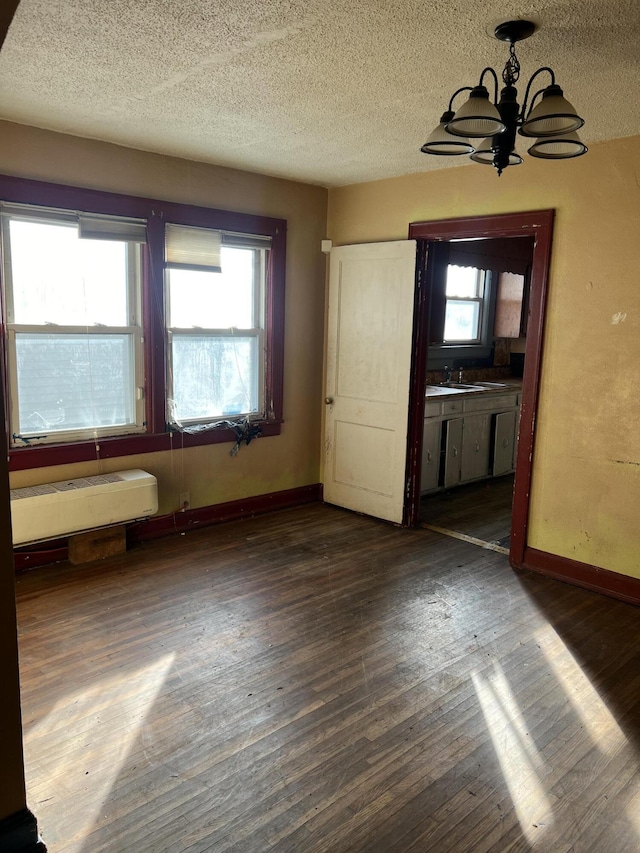 unfurnished dining area with a notable chandelier, dark wood-style floors, baseboards, and a textured ceiling